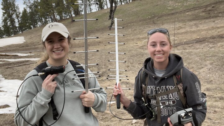 two field technicians hold radio telemetry equipment and smile at the camera